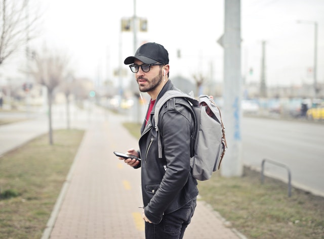 Muž s batohem na zádech držící v ruce telefon